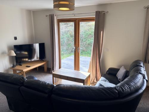 a living room with a leather couch and a sliding glass door at Abernethys Cottage in Connel