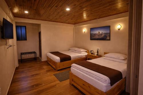 a hotel room with two beds and wooden floors at Kanchankanya Hill Resort in Takdāh