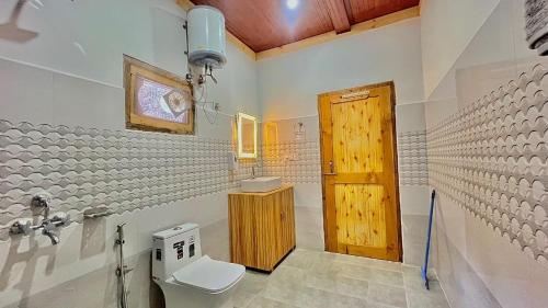 a bathroom with a toilet and a wooden door at Clifton Chapter Cottage Tirthan in Banjār