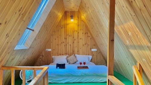 a bed in a wooden cabin with two glasses of wine at Clifton Chapter Cottage Tirthan in Banjār