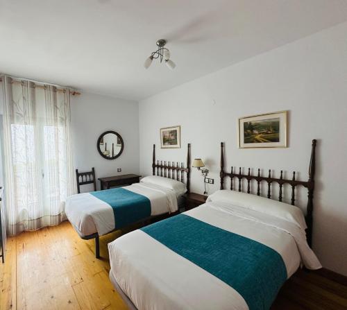 two beds in a room with white walls and wood floors at Hostal Pirineos Meliz in Bielsa