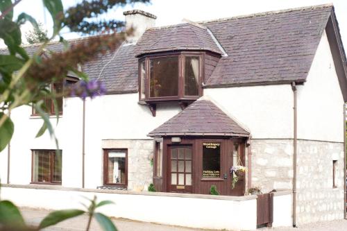 a white house with a brown roof and windows at Strathspey Cottage in Carrbridge