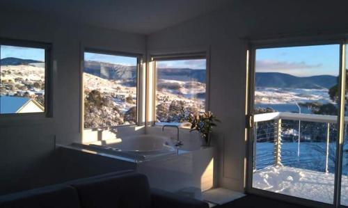 a bathroom with a tub and two large windows at Jindabyne Guest House in Jindabyne