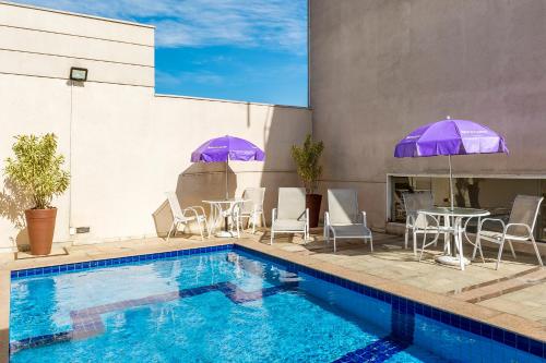 a pool with tables and chairs and purple umbrellas at Mercure Sao Paulo Naçoes Unidas in Sao Paulo