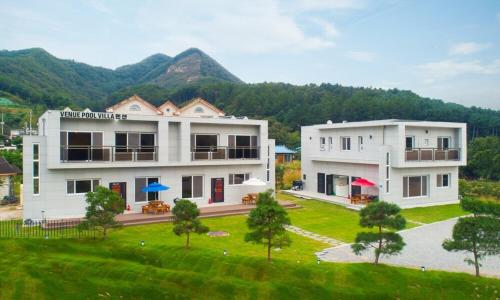 two white buildings with trees in front of a mountain at Chuncheon Venue Pool Villa August 19 in Chuncheon
