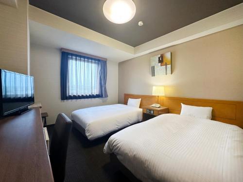 a hotel room with two beds and a flat screen tv at Hotel Route-Inn Tajimi Inter in Tajimi