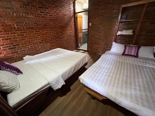 two beds in a room with a brick wall at ANOR Farmstay - Two Double Bed in Hue