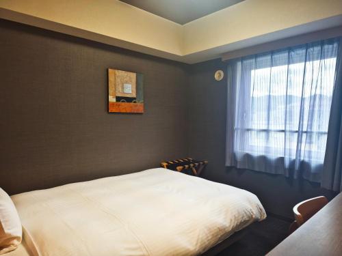 a bedroom with a white bed and a window at Hotel Route-Inn Hitachitaga in Hitachi