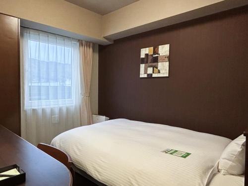 a bedroom with a white bed and a window at Hotel Route-Inn Dai-ni Suwa Inter in Suwa