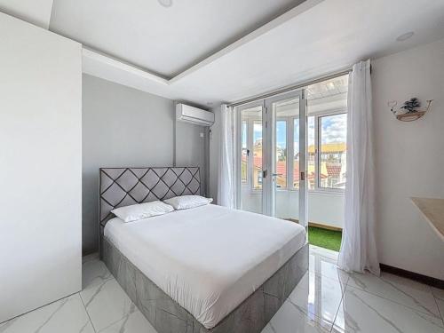 a white bedroom with a bed and a large window at Les Sables Roses Appartement in Flic-en-Flac