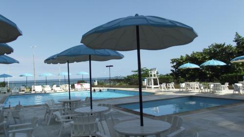 una piscina con mesas, sillas y sombrillas en BARRA BELLA PRAIA RESIDENCE - Internet 350mb -TV -AR - Vista mar - Piscina climatizada- HomeOficce, en Río de Janeiro