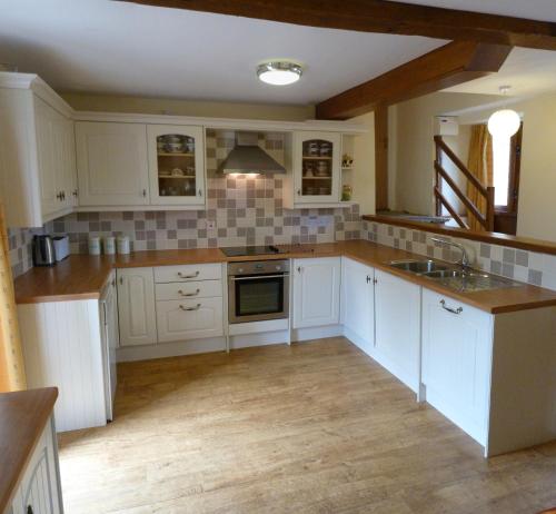 a kitchen with white cabinets and wooden floors at Beacons View Farm Cottages in Merthyr Cynog