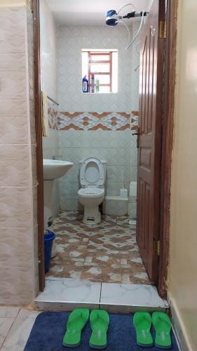 a bathroom with a toilet and a sink and green shoes at Unique place Studio Thika in Thika