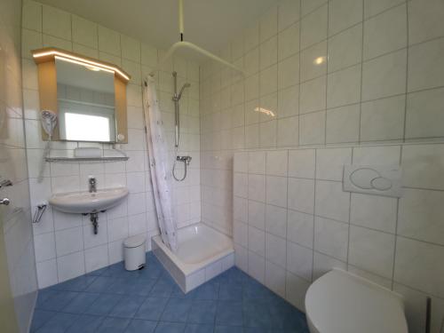 a white tiled bathroom with a sink and a toilet at Schirmer`s Hotelino in Röhrmoos