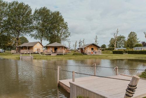 a group of cottages on a lake with a dock at Safaritent Ranger Lodge in Kesteren