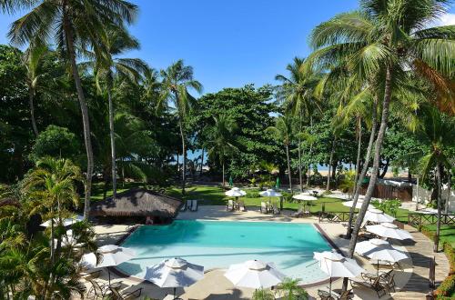 a swimming pool with umbrellas and tables and palm trees at Iara Beach Hotel Boutique in Salvador