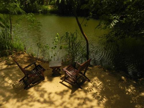 three wooden benches sitting next to a body of water at Makulu Safari Camping in Udawalawe