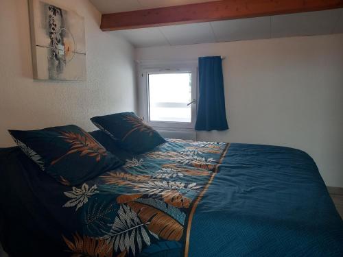 a bedroom with a bed with a blue comforter and a window at La Petite de Cayola in Talmont
