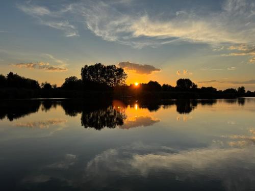 a sunset over a lake with the reflection of the sky at Waterside Cottage in Nagyrév