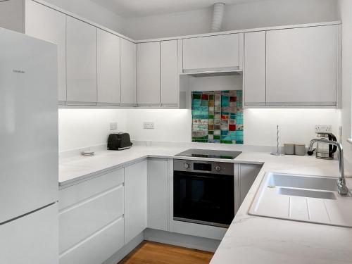 a white kitchen with white cabinets and a sink at White Sands Cottage in Weymouth
