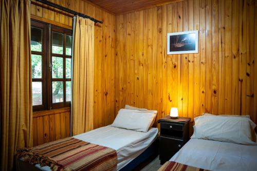 two beds in a room with wooden walls and a window at El Descanso Iguazú by DOT Cabana in Puerto Iguazú