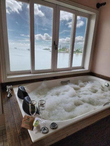a bath tub with a window and a glass of wine at Pousada Pedra das Tartarugas in São Francisco do Sul
