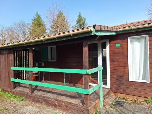 a wooden house with a green railing on the porch at Camping Onlycamp Les Bords de Lyonne in Saint-Jean-en-Royans