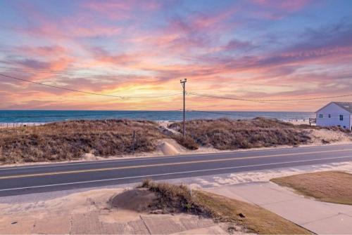 an empty road in front of the ocean at sunset at Pelican Watch - Kitty Hawk MP 3, 16 Yards to Beach, Ocean View, Pool, Hot Tub, Pool Table, Flex Stays in Kitty Hawk