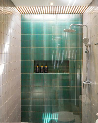 a bathroom with a green tiled shower with bottles on a shelf at Jisa Sidemen in Sidemen
