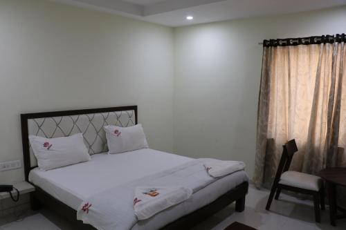 a bedroom with a bed with white sheets and a chair at Hotel Satkar in Amalāpuram