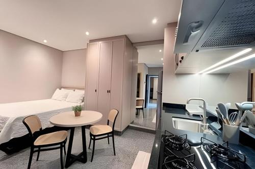a bedroom with a bed and a table and a kitchen at Santorini Urban Studio • conforto e estilo in Londrina