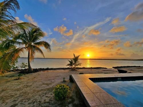 a sunset on a beach with palm trees and a swimming pool at Grand Sunset Decks Luxury Home on the Lagoon in Maya Beach