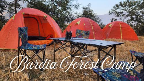 a table and chairs in front of three tents at Bardia Forest Camp in Bardiyā
