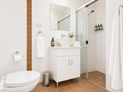 a white bathroom with a toilet and a sink at Relaxing 2BR Split-Level Home in Wahroonga in Waitara