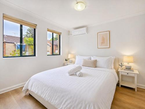 a white bedroom with a large white bed and two windows at Relaxing 2BR Split-Level Home in Wahroonga in Waitara