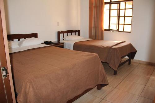 two beds in a hotel room with a window at hotel turistico in Huaraz
