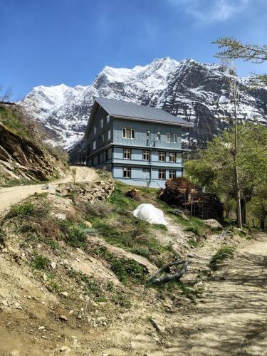 a building on a hill with a snow covered mountain at beheney Homestay gondhla in Kyelang