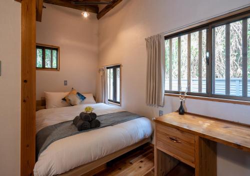 a bedroom with a bed and a desk and windows at simAsim Cottage Kouri in Nakijin