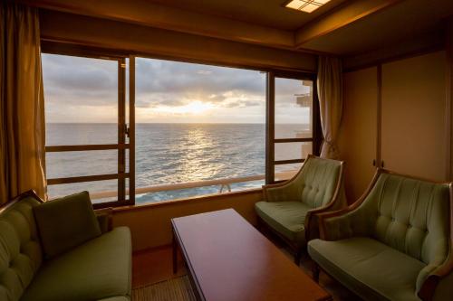 a room with two chairs and a window with the ocean at Bousui in Higashiizu