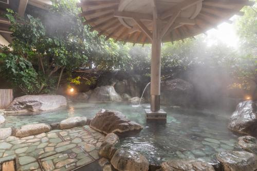 an outdoor hot tub with an umbrella and rocks at Bousui in Higashiizu