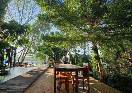 Ein Holztisch und Stühle auf einer Terrasse mit Bäumen in der Unterkunft Amphawa Hideaway in Amphawa