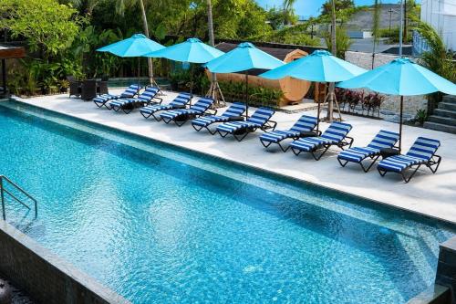 a swimming pool with blue chairs and umbrellas at Watermark Hotel & Spa Bali in Jimbaran