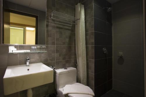 a bathroom with a toilet and a sink and a mirror at Fives Hotel Desaru in Desaru