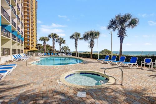 a swimming pool with chairs and palm trees and a building at Carolinian Beach Resort in Myrtle Beach