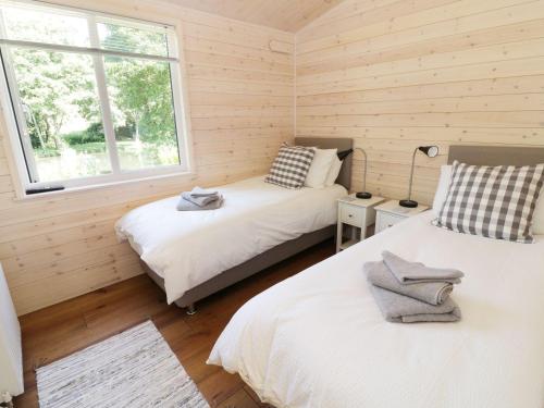 two beds in a room with wooden walls and a window at Kingfisher in Ross on Wye
