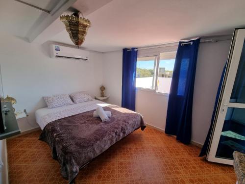 a bedroom with a bed and a window with blue curtains at Plage El Haouzia in El Jadida