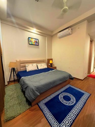 a bedroom with a bed with blue sheets and a rug at ITC Grand Stay in Greater Noida
