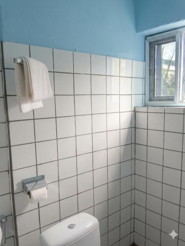 a white tiled bathroom with a toilet and a window at Madibak Hotel Limbe in Limbe