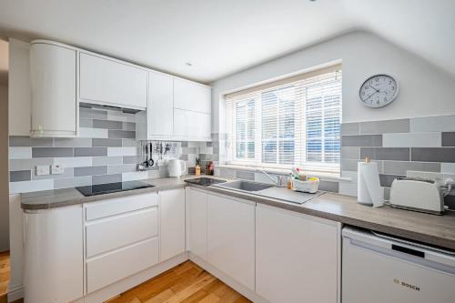 a kitchen with white cabinets and a clock on the wall at Comfortable Cottage with Decking in Castle Cary in Castle Cary