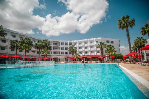 a large pool with red umbrellas in front of a hotel at Houda Yasmine Marina & SPA in Hammamet